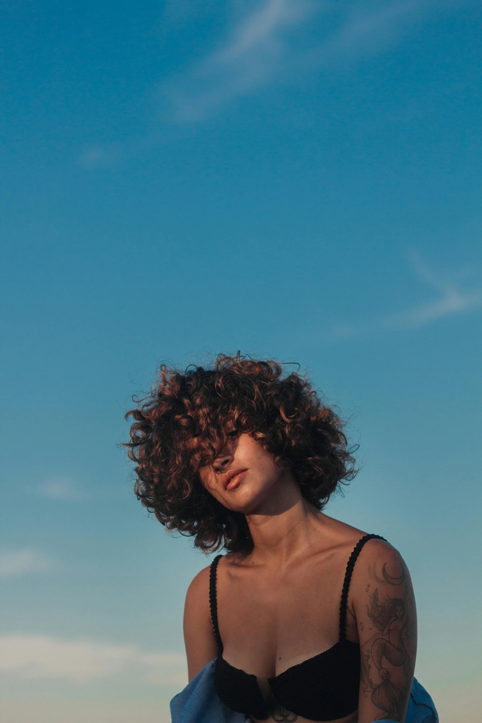 a woman in a bikini sitting on a beach, an album cover, inspired by Elsa Bleda, trending on pexels, curly middle part haircut, skies, profile portrait, mixed race