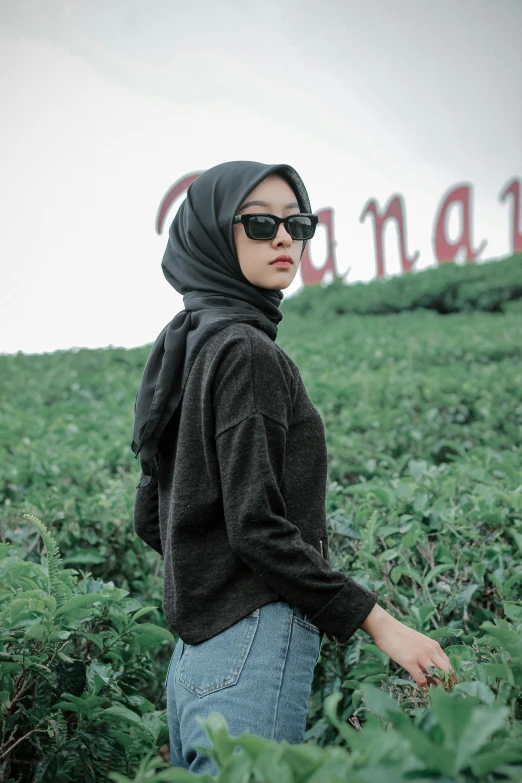 a woman standing in the middle of a field, unsplash, hurufiyya, wearing a black sweater, jakarta, with sunglasses, square