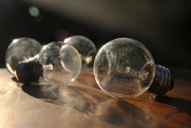 a group of light bulbs sitting on top of a wooden table, a macro photograph, by David Simpson, unsplash, glass spheres, sun dappled, silver light, lit from the side