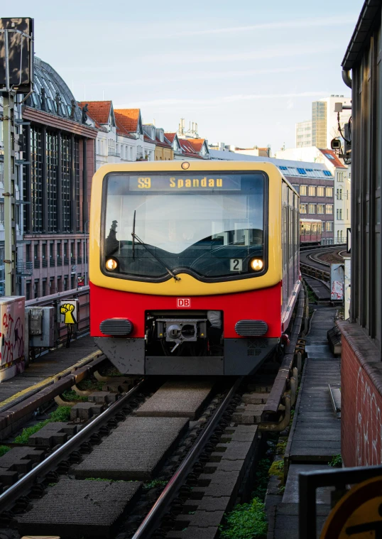 a red and yellow train traveling down train tracks, by Werner Gutzeit, instagram, city in background, slide show, square, no - text no - logo