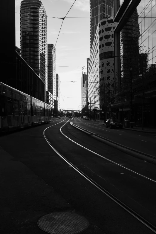 a train traveling through a city next to tall buildings, a black and white photo, postminimalism, north melbourne street, empty road in the middle, light traces, square lines