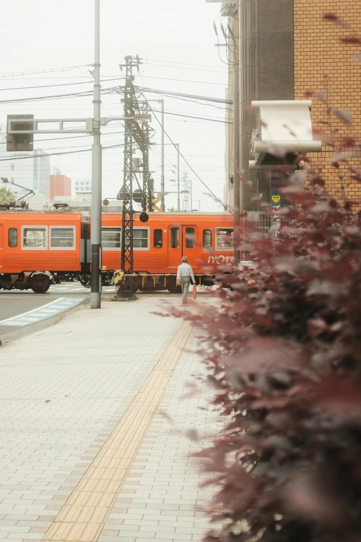 an orange train traveling down train tracks next to a building, a picture, unsplash, mingei, 4k”, movie set”, grain”