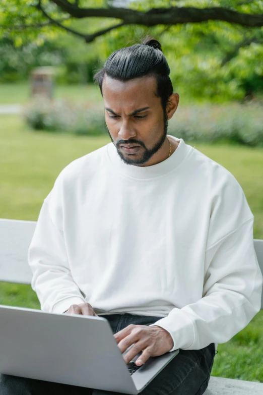 a man sitting on a bench using a laptop, trending on reddit, wearing a white sweater, indian, looking serious, in a garden