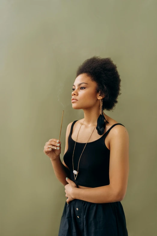 a woman standing in front of a green wall, trending on pexels, renaissance, black whispy smoke, natural hair, holding a cane, black jewelry