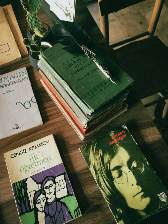 a pile of books sitting on top of a wooden table, poster art, inspired by Károly Ferenczy, trending on unsplash, portrait of jim morrison, green shades, high angle close up shot, old john lennon