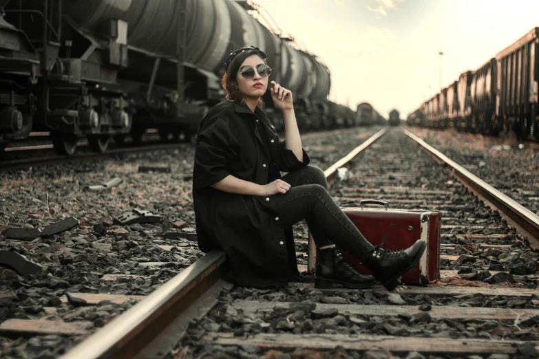 a woman sitting on train tracks talking on a cell phone, a portrait, by Lucia Peka, pexels contest winner, steampunk clothes, in suitcase, wearing black stylish clothing, blank