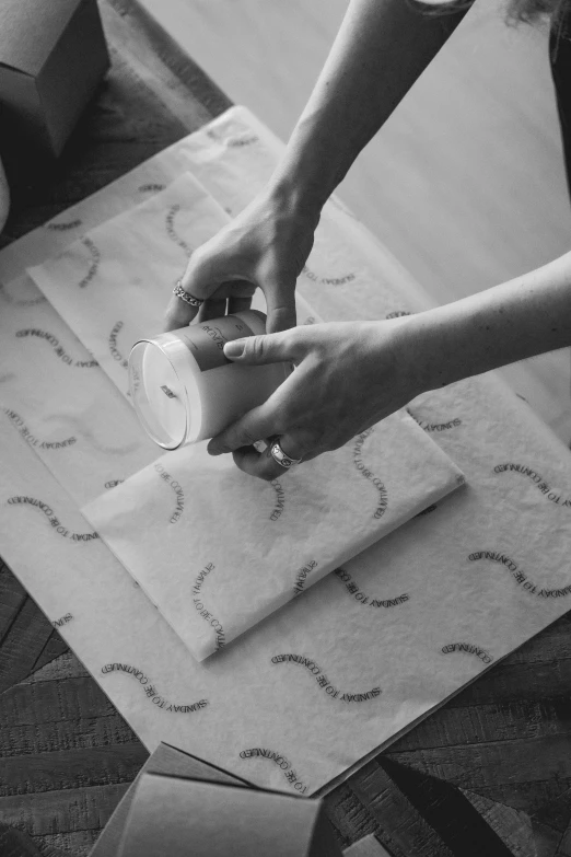 two hands on top of a box while a person wraps the wrapping