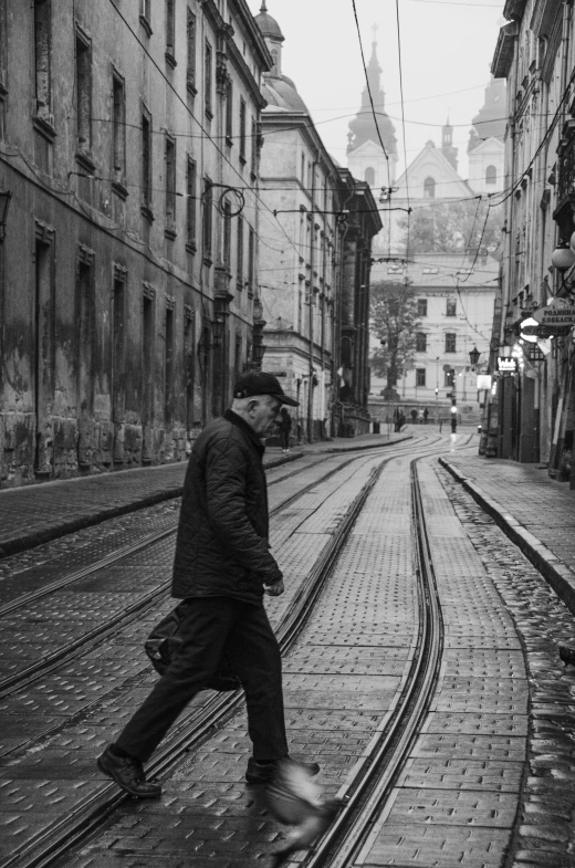 a black and white photo of a man walking down a street, by Tamas Galambos, unsplash contest winner, lviv historic centre, trams, cold mood, evening time