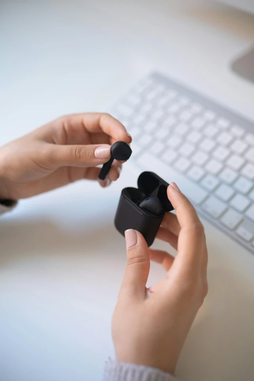 a close up of a person holding an object in front of a keyboard, earbuds, all black matte product, silicone skin, scientific