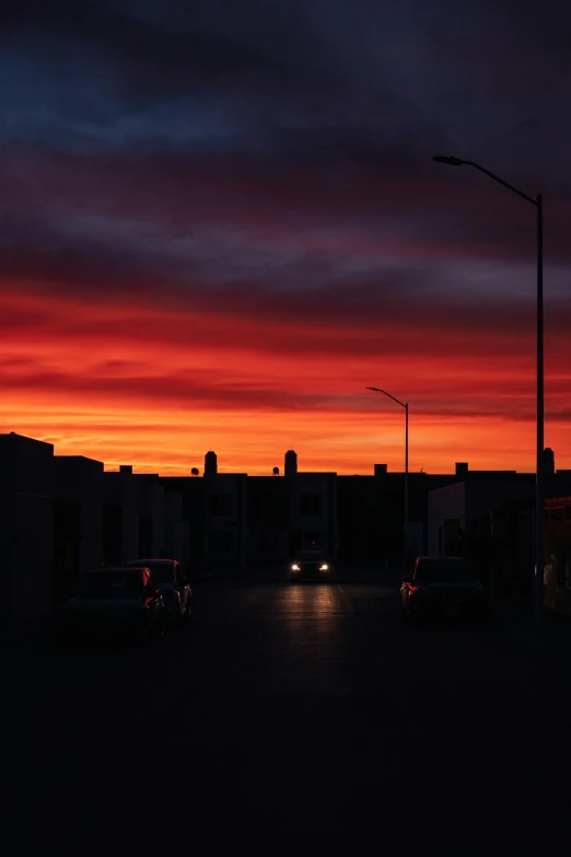 a sunset view from a dark parking lot with buildings and street lamps in the background