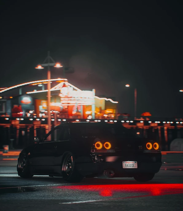 a black car is in front of the ferris wheel at night