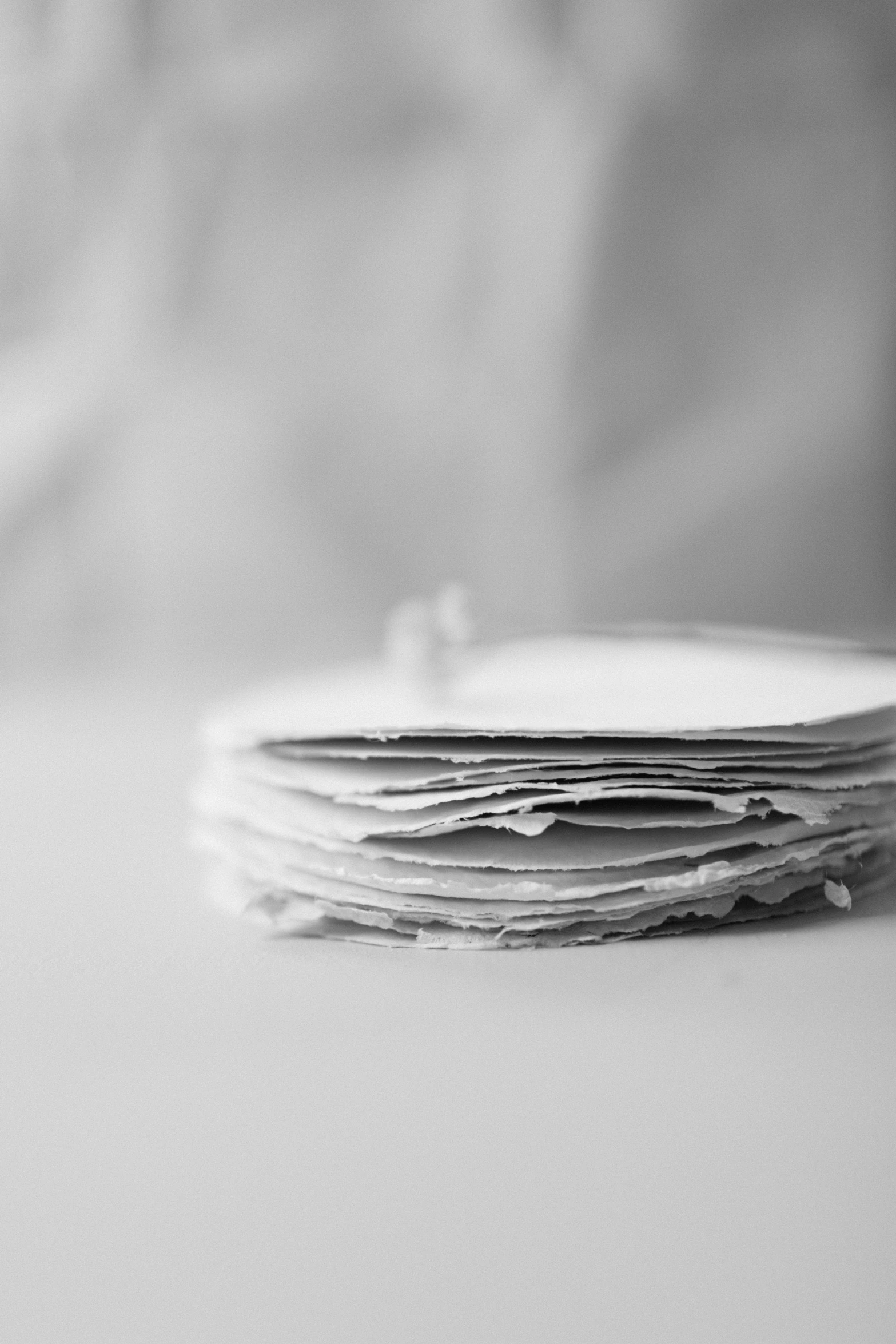 a stack of papers sitting on top of a table, a black and white photo, by Matthias Weischer, pancakes, delicate details, round-cropped, torn paper edges