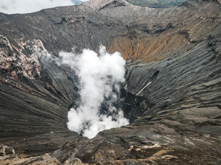 steam rises from the ventulating of a crater with mountains in the background