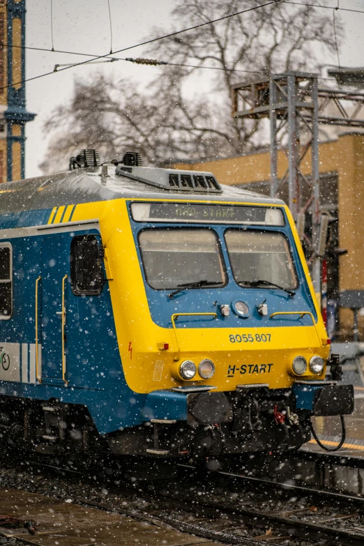 a blue and yellow train traveling down train tracks, by Sven Erixson, pexels contest winner, snowing outside, square, anato finnstark. front view, technical