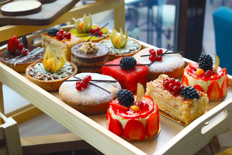 a tray of desserts sitting on top of a table, mesmerising, on a wooden tray, bright day, cakes