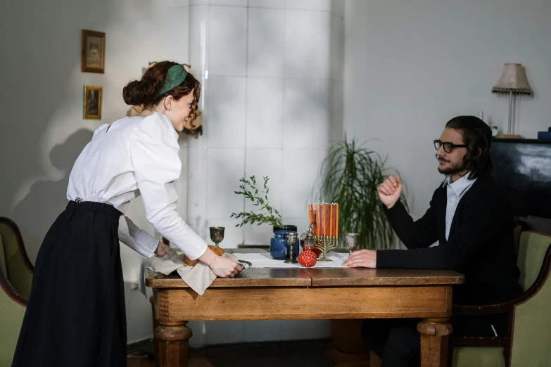 a man and woman sitting at a wooden table in front of a plant