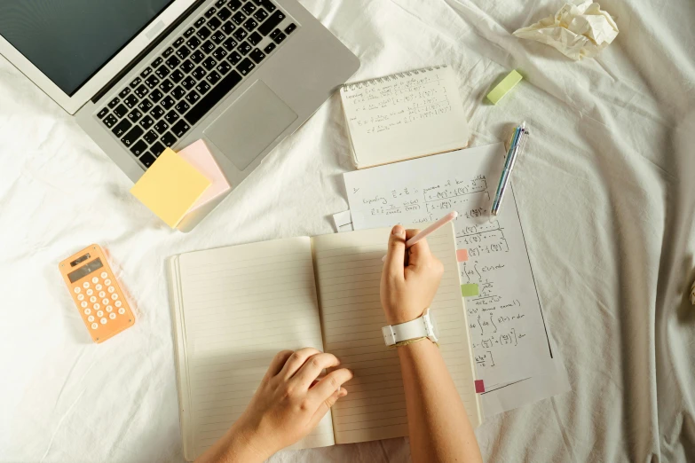 a woman sitting on top of a bed next to a laptop computer, trending on pexels, academic art, with notes, high angle shot, educational supplies, background image