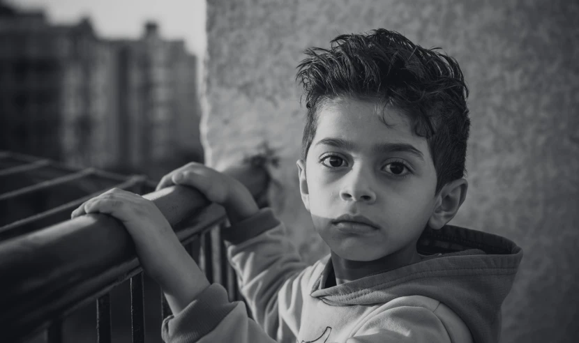 a black and white photo of a young boy, a black and white photo, pexels contest winner, realism, from egypt, urban in background, serious expressions, young and cute