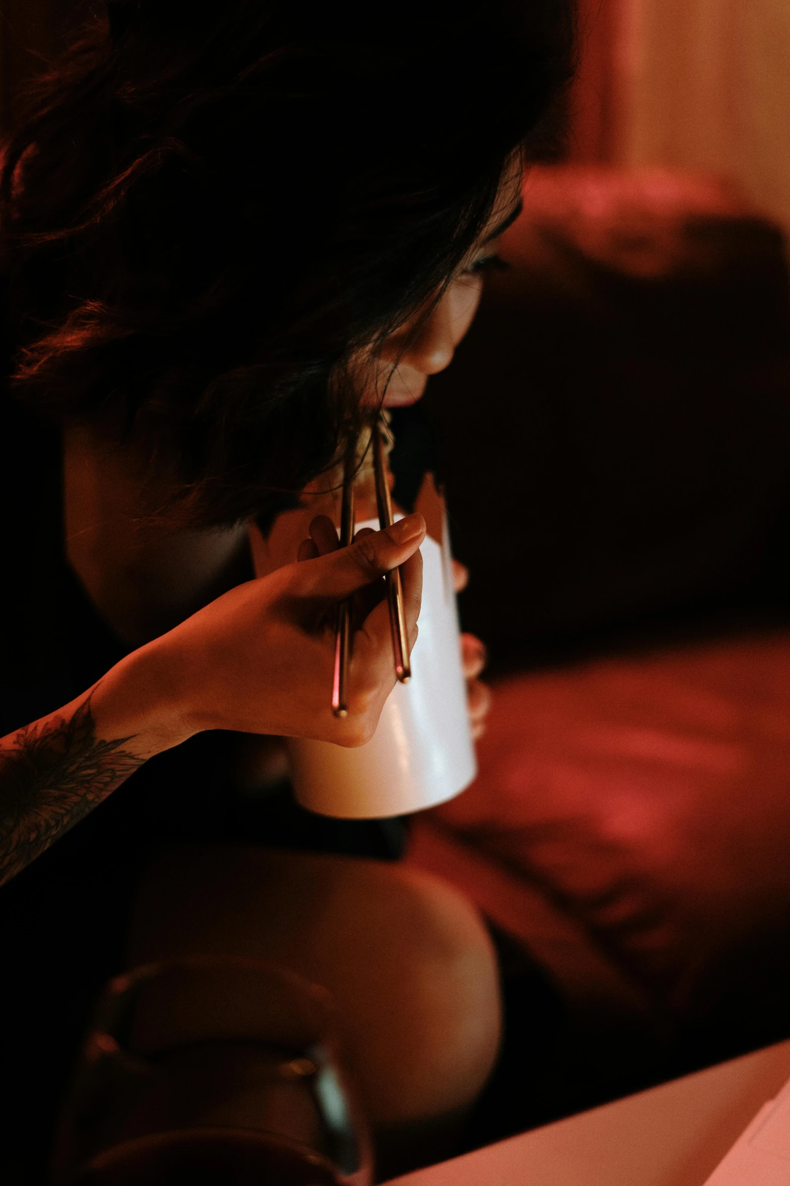 a woman sitting on a couch with a cup of coffee, inspired by Elsa Bleda, smoking a magical bong, low lighting, connection rituals, holding a bottle of arak