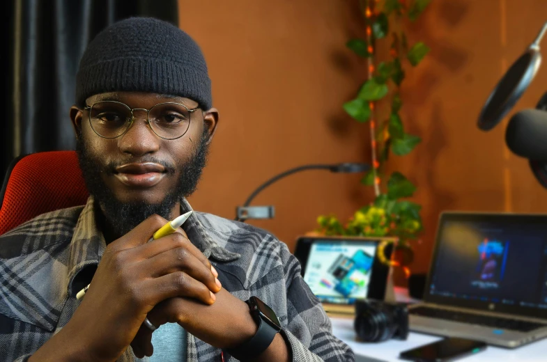 a man sitting in front of a laptop computer, by Chinwe Chukwuogo-Roy, pexels contest winner, afrofuturism, holding a small vape, looking straight to camera, engineer, portrait of tall