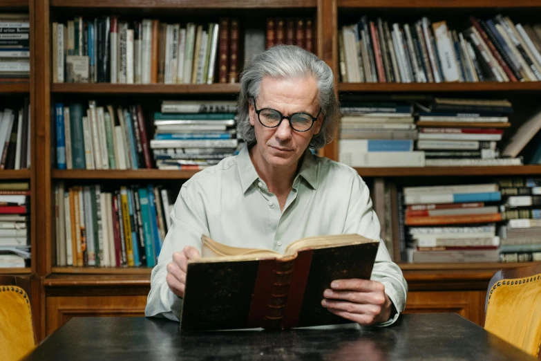 a man sitting at a table reading a book, by James Morris, dark grey haired man, lachlan bailey, portrait image, wim wenders