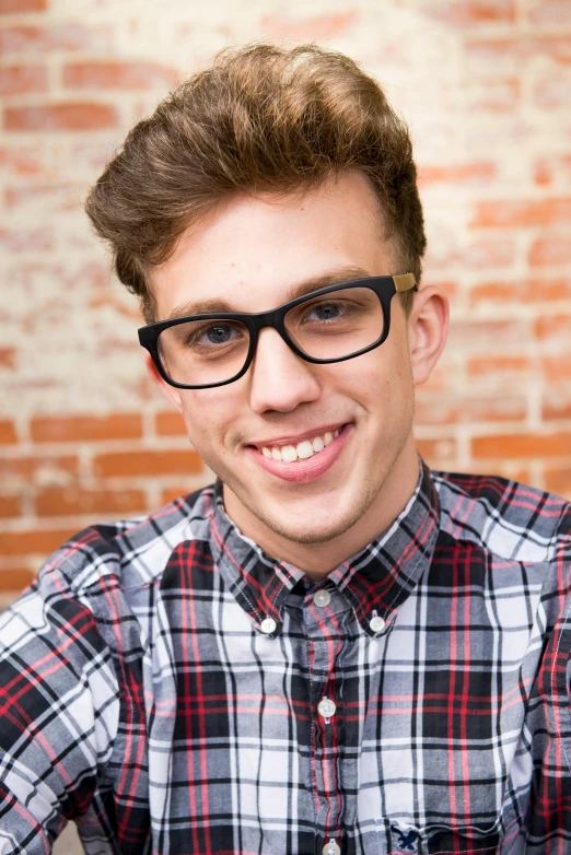 a young man taking a selfie in front of a brick wall, inspired by Ryan Pancoast, square rimmed glasses, wearing plaid shirt, promo image, portrait close up of guy