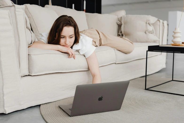 a woman laying on the floor in front of a laptop, trending on pexels, couch, woman with braided brown hair, low quality photo, concentration