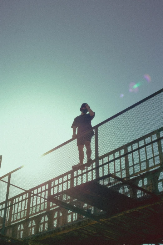 a man standing on top of a metal railing, inspired by Elsa Bleda, happening, anamorphic lens flare, crane shot, ignant, low quality photo