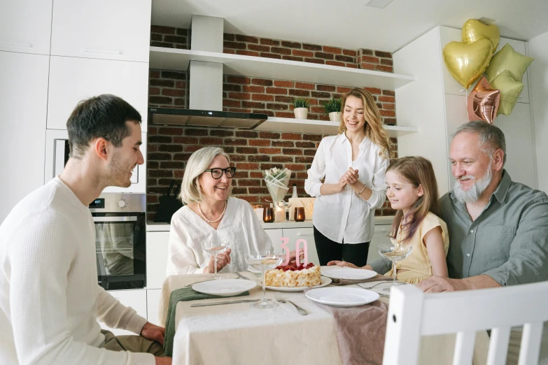 a group of people sitting around a table with a cake, white kitchen table, profile image, 1 petapixel image, families playing