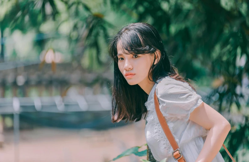 a woman in a white shirt holding a brown bag, by Tan Ting-pho, pexels contest winner, looking off into the distance, korean girl, girl cute-fine-face, standing in a botanical garden