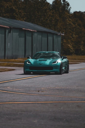 a turquoise colored sports car is on an asphalt road