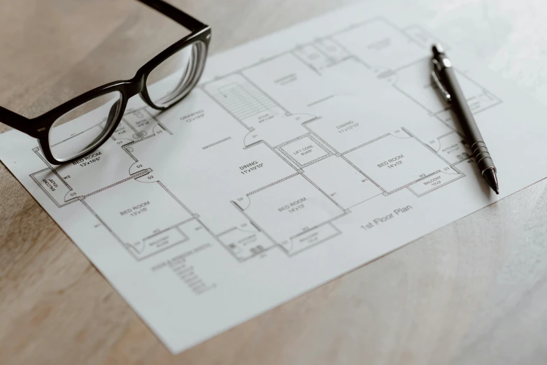 a pen, eyeglasses and a blueprint on a table