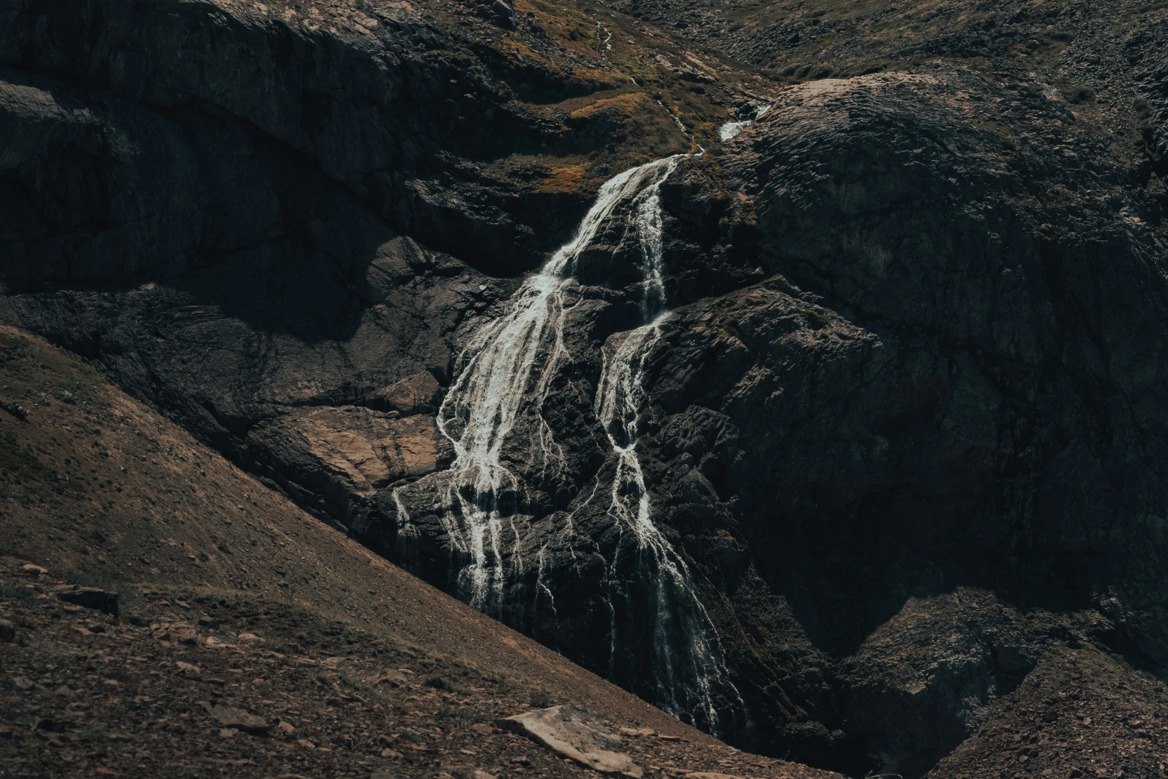 a person walking up a steep hillside by a small waterfall