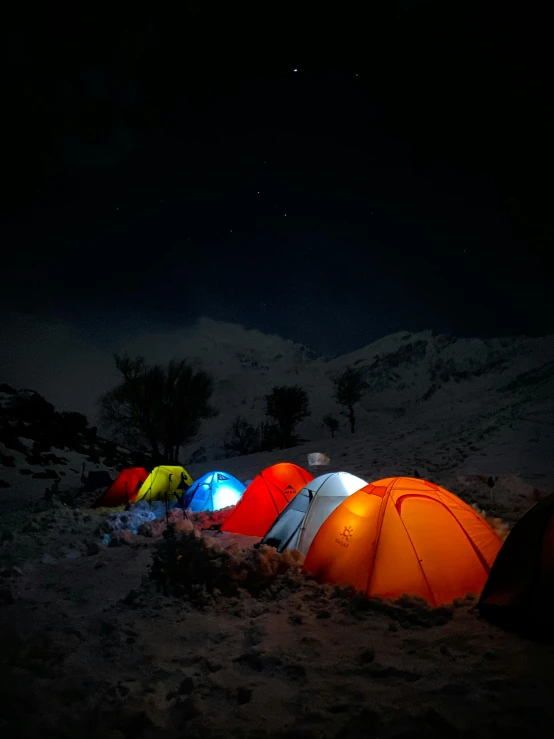 a group of tents sitting on top of a snow covered ground, during the night, at night time