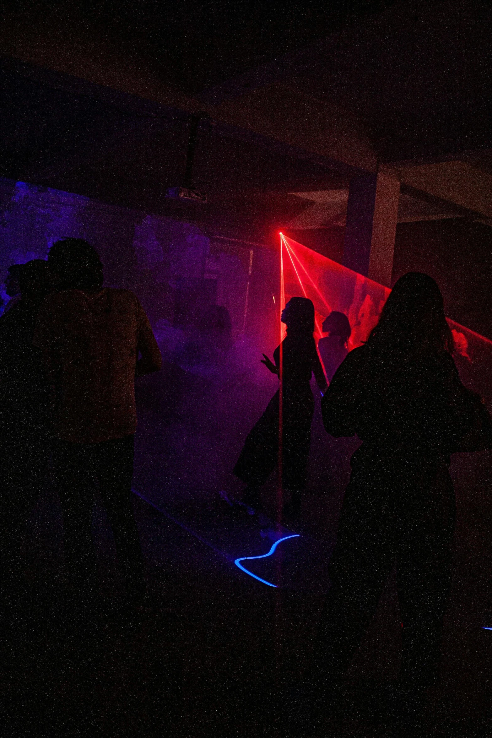 a group of people standing in a dark room, interactive art, red lasers, line dancing at a party, masked person in corner, neon colored haze