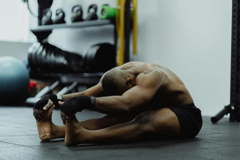 a man sitting on the ground in a gym, pexels contest winner, hurufiyya, bending down slightly, man is with black skin, lachlan bailey, long tail