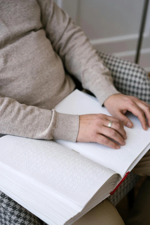 a woman sitting in a chair holding a book, by David Donaldson, trending on unsplash, close-up of thin soft hand, wearing a white sweater, non-binary, 15081959 21121991 01012000 4k