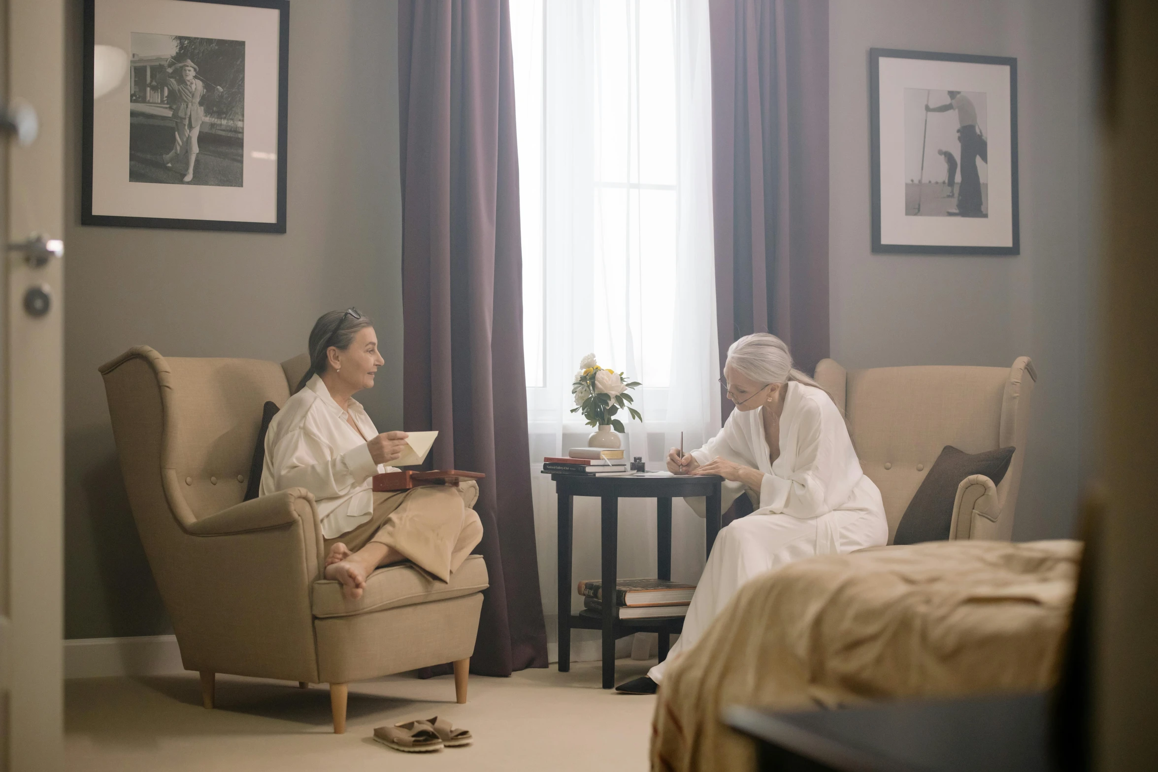 two ladies are sitting on couches near a window