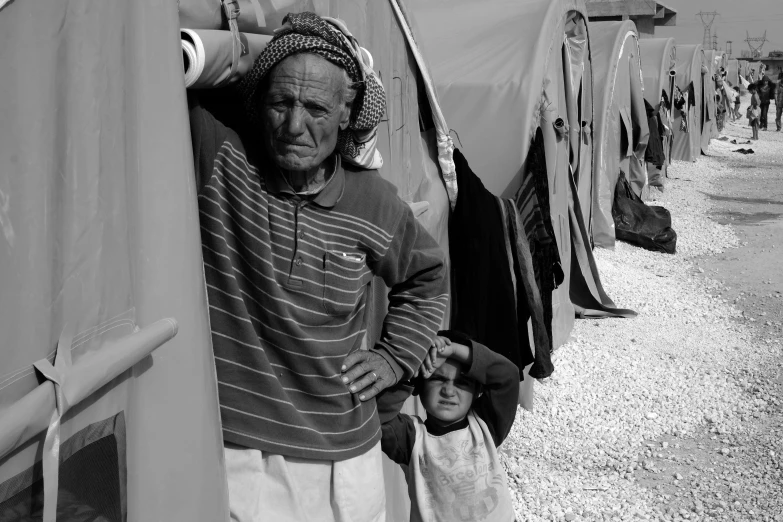 a black and white photo of a man leaning against a tent, a black and white photo, by Ibrahim Kodra, with a kid, looking old, bags under his eyes, monochrome:-2