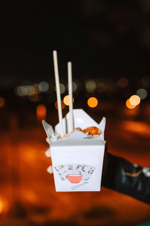 a person holding a box of food with chopsticks in it, city lights, white, tall, chicken