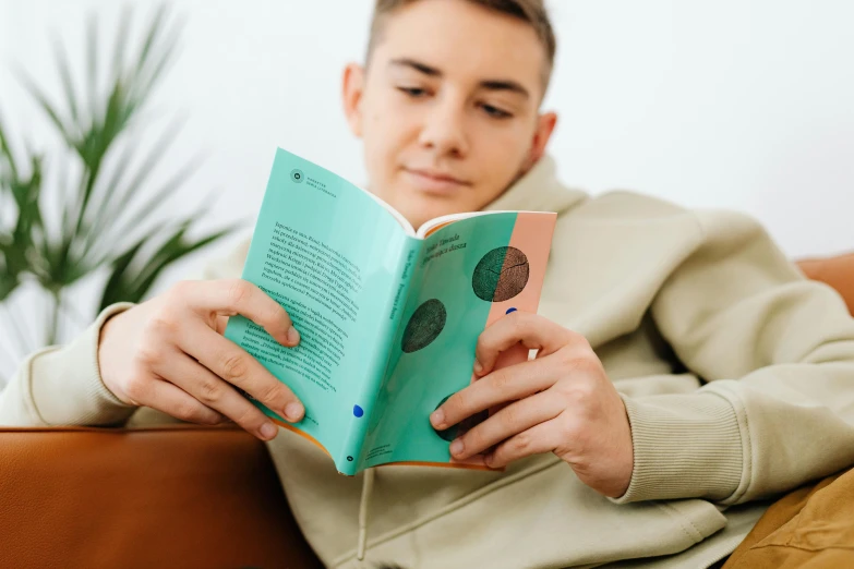 a man sitting on a couch reading a book, by Carey Morris, trending on pexels, mannerism, brand colours are green and blue, teenage boy, sustainable materials, with book of science