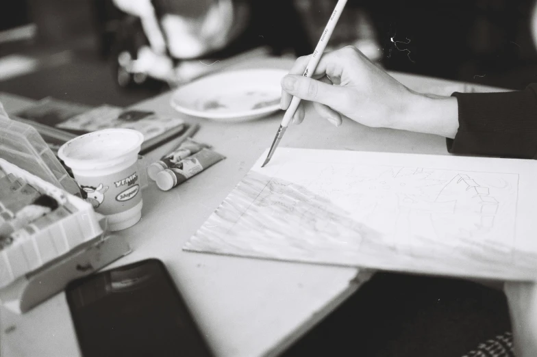 a person sitting at a table with a pencil and paper, pexels contest winner, process art, black and white paint, fan favorite, instagram story, holding a paintbrush