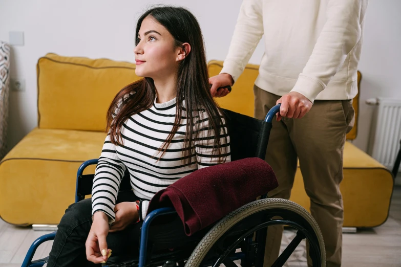 a woman sitting in a wheel chair next to a man, trending on pexels, hurufiyya, leaving a room, woman with braided brown hair, plain background, looking her shoulder