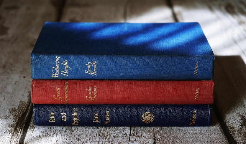 a stack of three books sitting on top of a wooden table, inspired by Edward Armitage, navy, embossed, medium-shot
