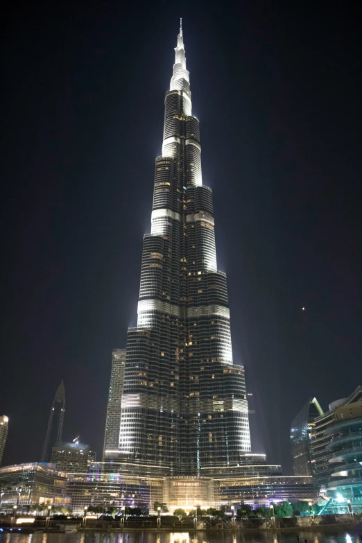 the burj tower lit up at night, next to the river