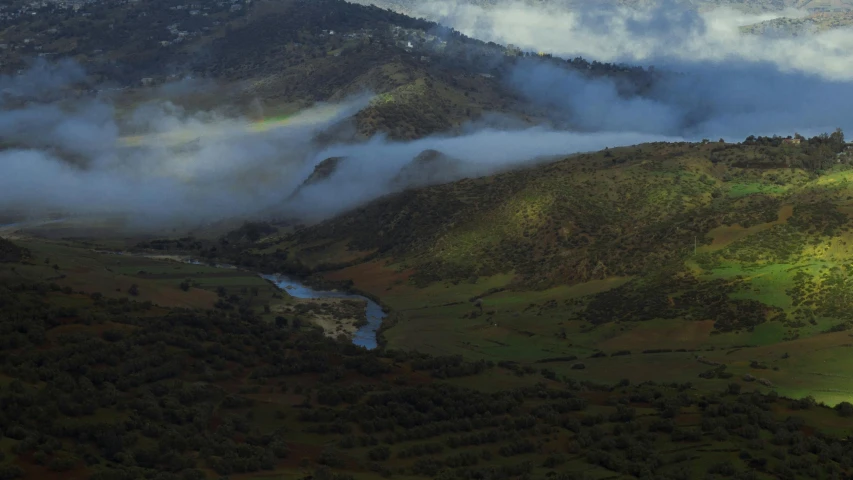 some trees and mountains with a river and clouds