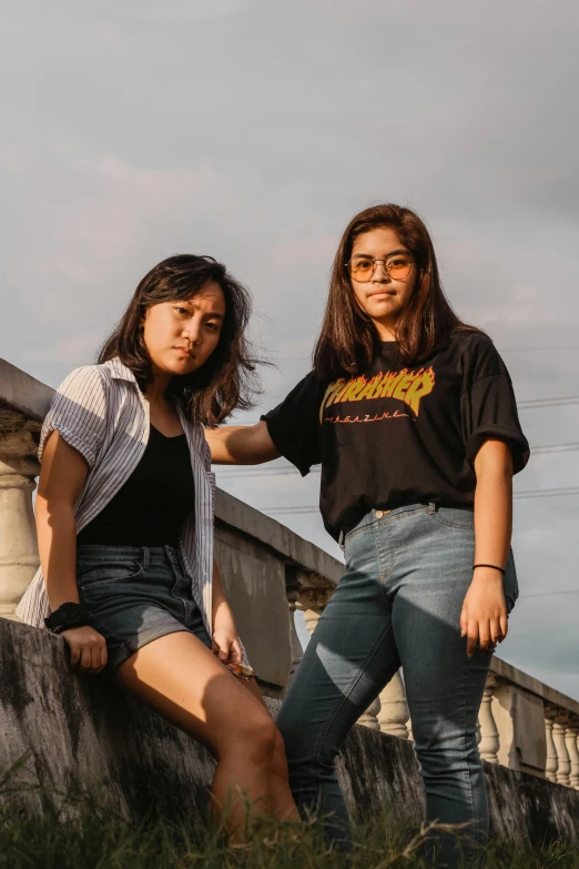 two women standing in the grass on a bridge