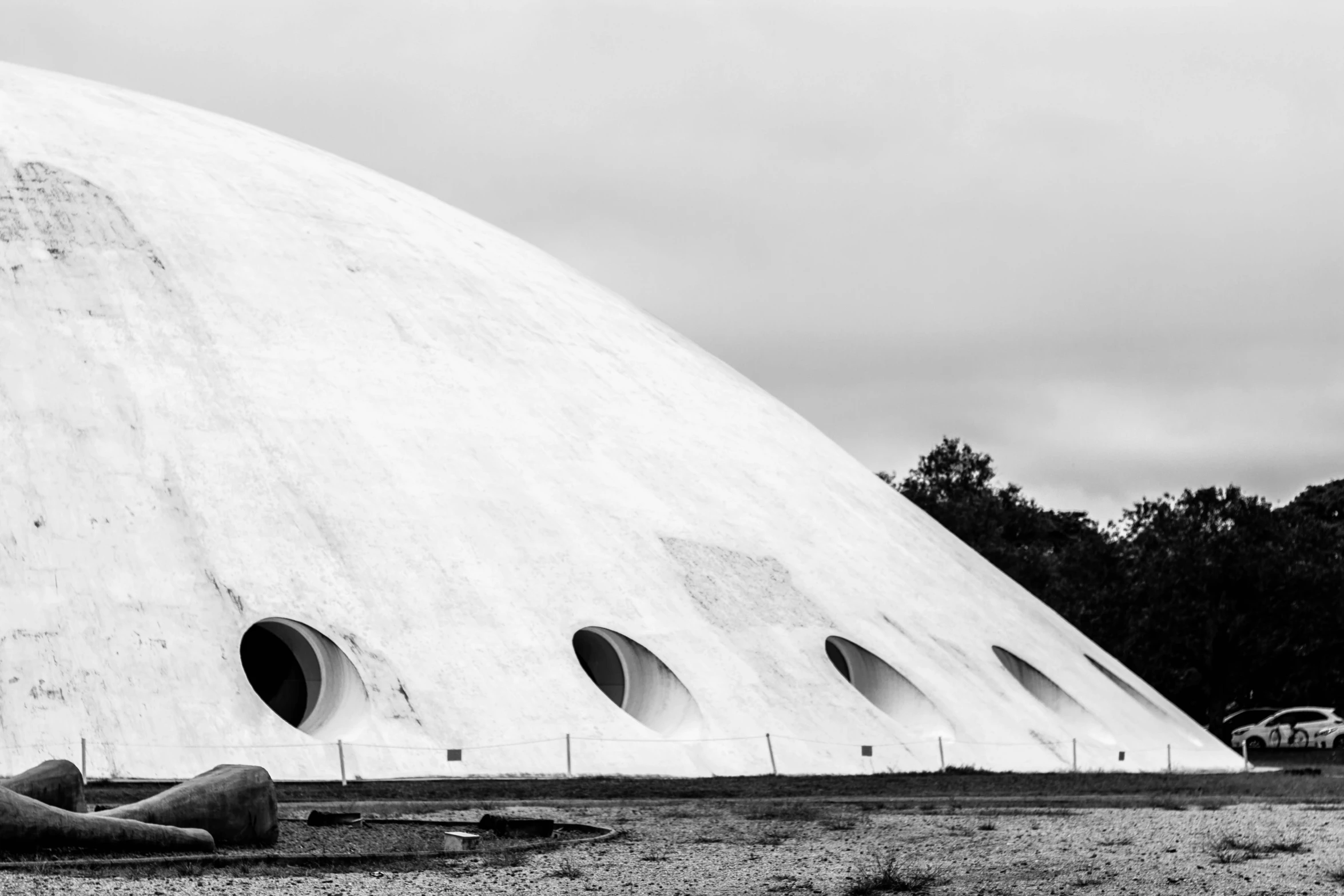 a man laying on the ground in front of a building, a black and white photo, inspired by Willem Claeszoon Heda, unsplash contest winner, brutalism, futuristic dome, space ship cemetery outer space, white stone, photo of a huge theaterstage