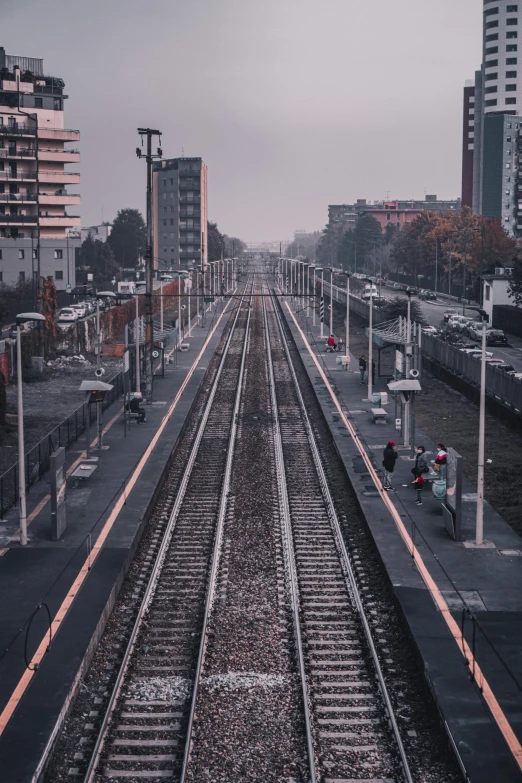 a train traveling down train tracks next to tall buildings, by Alessandro Allori, unsplash contest winner, sparsely populated, square, late morning, lots of people