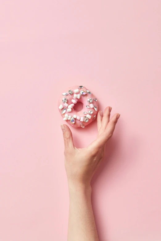 a woman's hand holding a donut on a pink background, inspired by Pearl Frush, trending on pexels, floating crystals, profile image, on grey background, made out of sweets